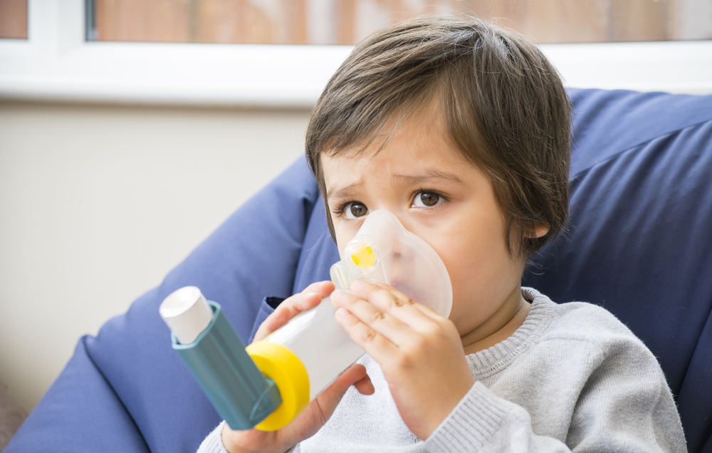 A boy have a problem with chest coughing holding inhaler mask by him self, Kid using the volumtic for breathing treatment, Healthcare and medicine concept