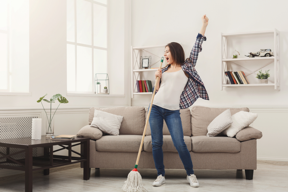 Happy woman cleaning home, singing at mop like at microphone and having fun, copy space. Housework, chores concept